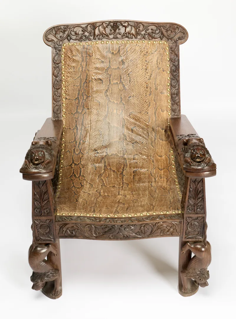 Profusely carved plantation armchair with lion arm terminals, extending leg rests and reptile-skin upholstery