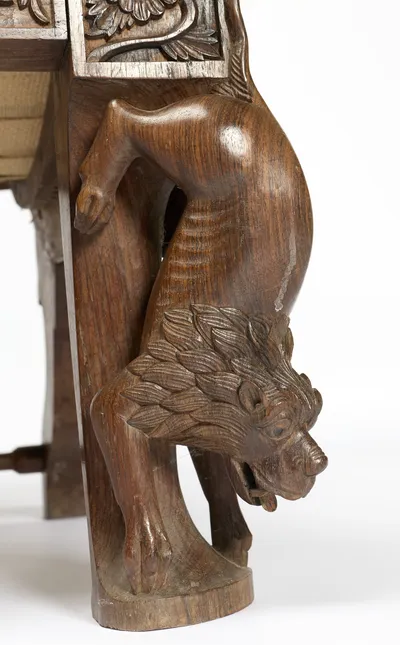 A maned animal climbs head-first down the leg, its hindquarters at the seat rail and its muzzle near the foot.