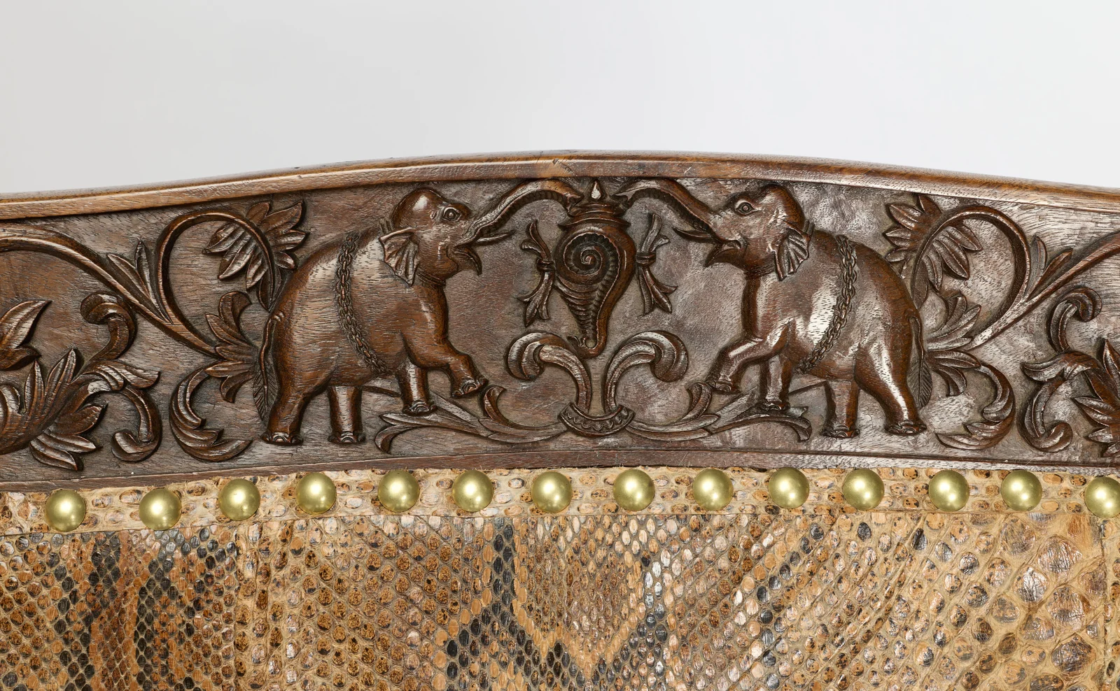 Two elephants wearing carved chains raise their trunks to a central spiral-fluted motif amid acanthus scrolls, above a close run of brass studs.