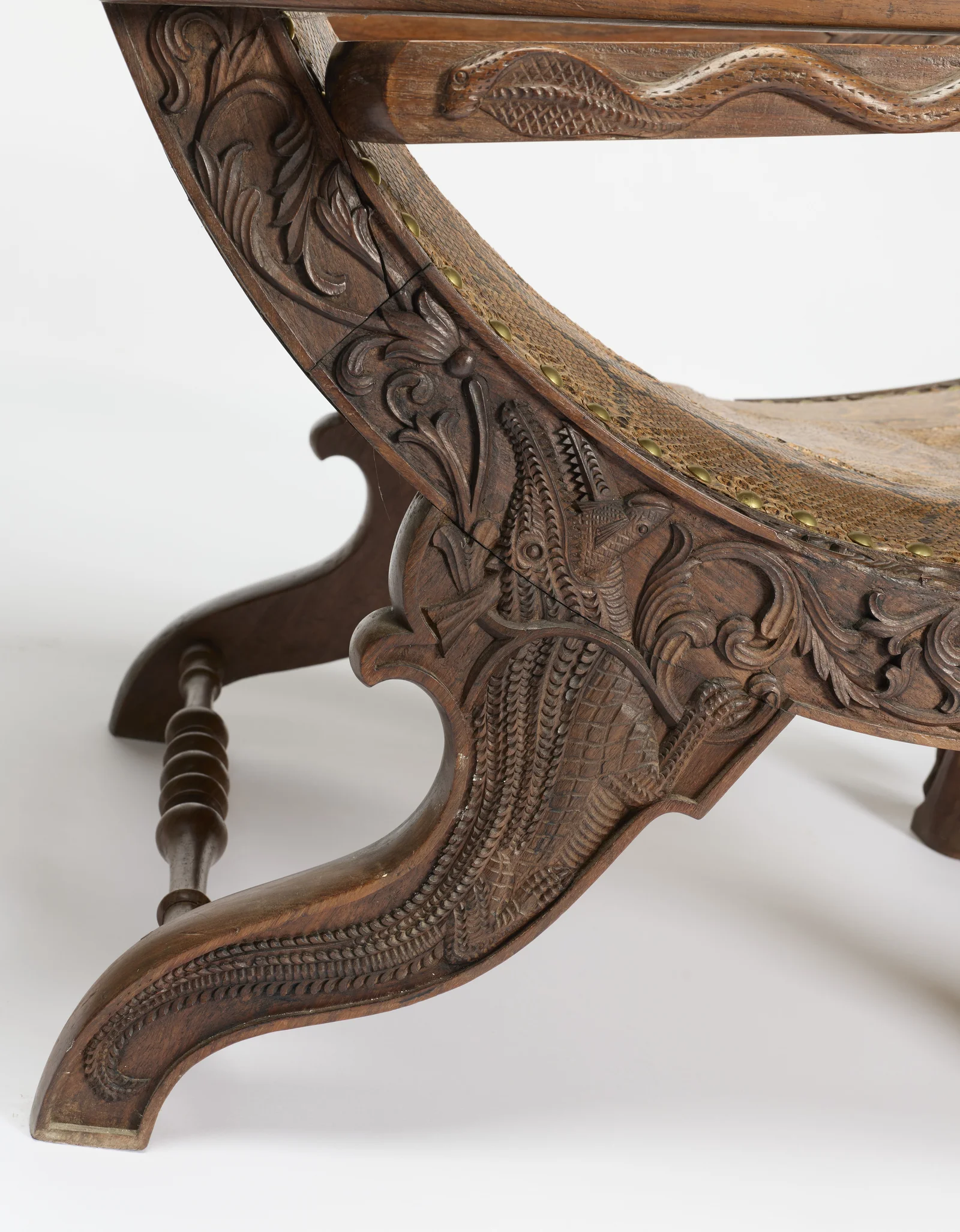 A crocodile with cross-hatched scales and toothed jaws winds through scrolls on the shaped support, a snake carved along the rail above.
