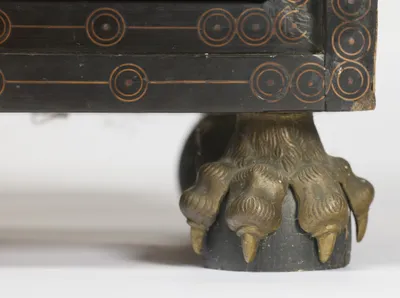 A cast metal paw with raised claws grips an ebonised dome beneath the circle-inlaid base rail.