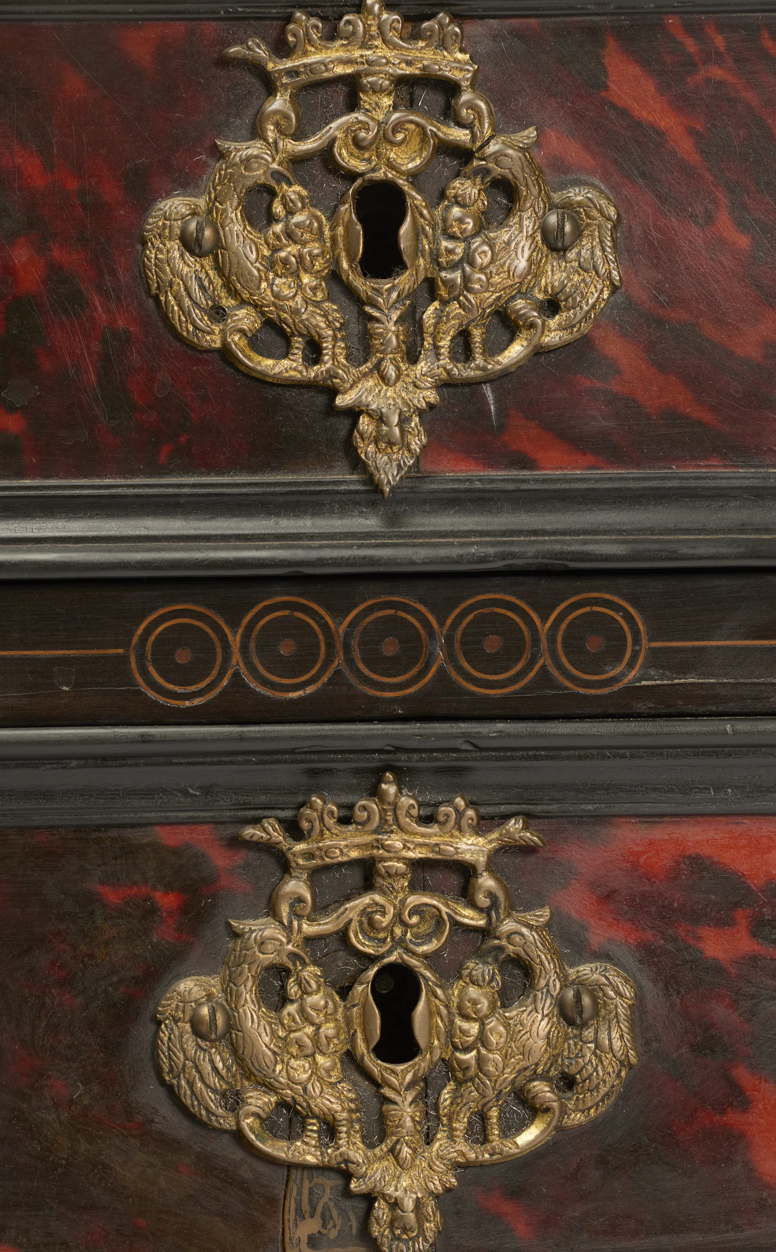 Two keyhole plates cast as paired birds beneath a crown, set on mottled red panels divided by a band of circle inlay.