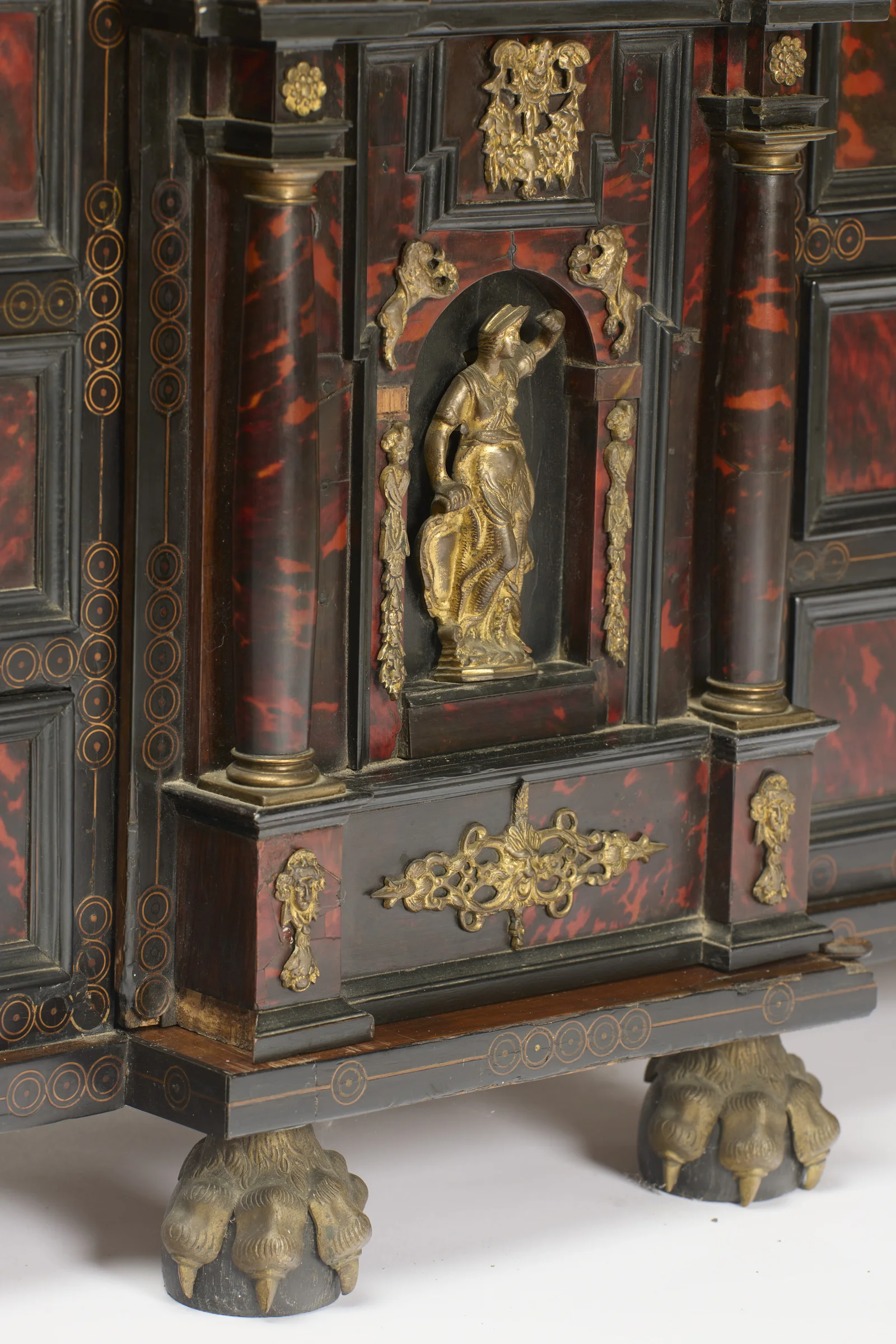 A gilt-metal figure of a woman stands in an arched recess between columns; gilt lion masks perch on the arch, garland drops hang beside her and a pierced scrolling mount fills the panel below.