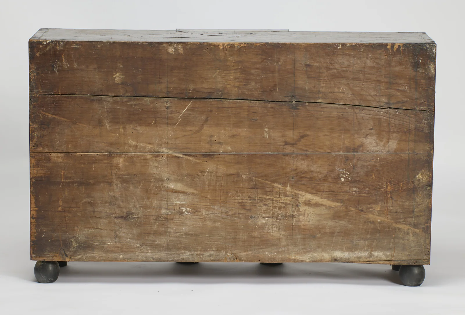 Plain boards run the full width of the back, scuffed and marked with age, over ebonised ball feet.