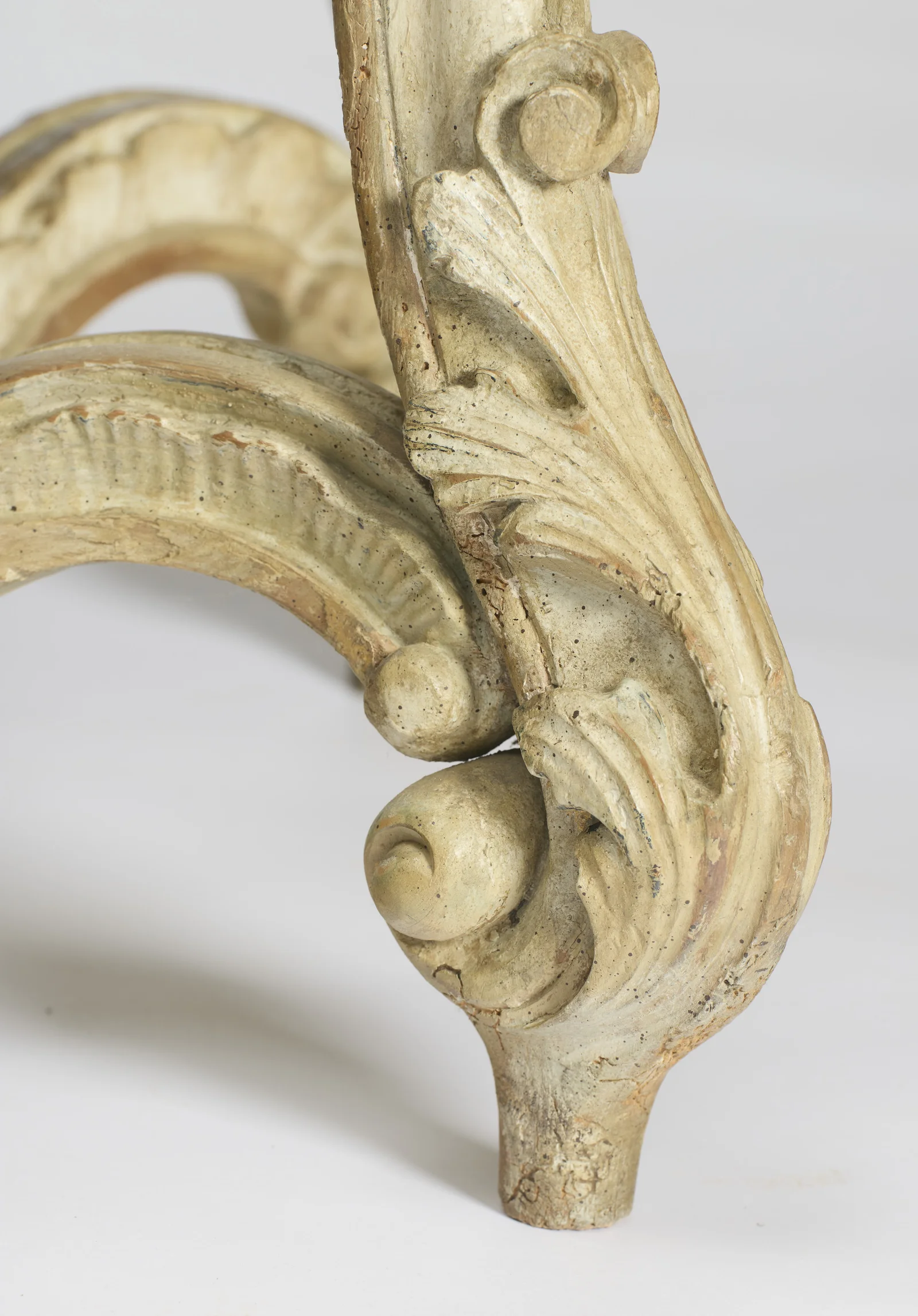 Tight detail of one scroll foot showing the leaf carving, speckled old paint and the bare toe where the finish has worn.