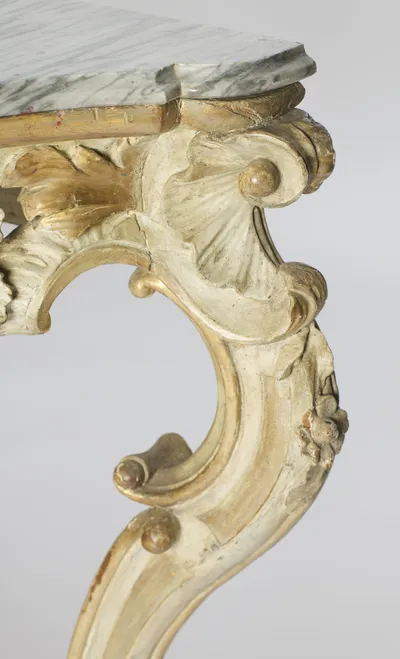The grey veined marble over its gilt border, where a reddish ground shows through the worn gilding above the shell-carved knee.