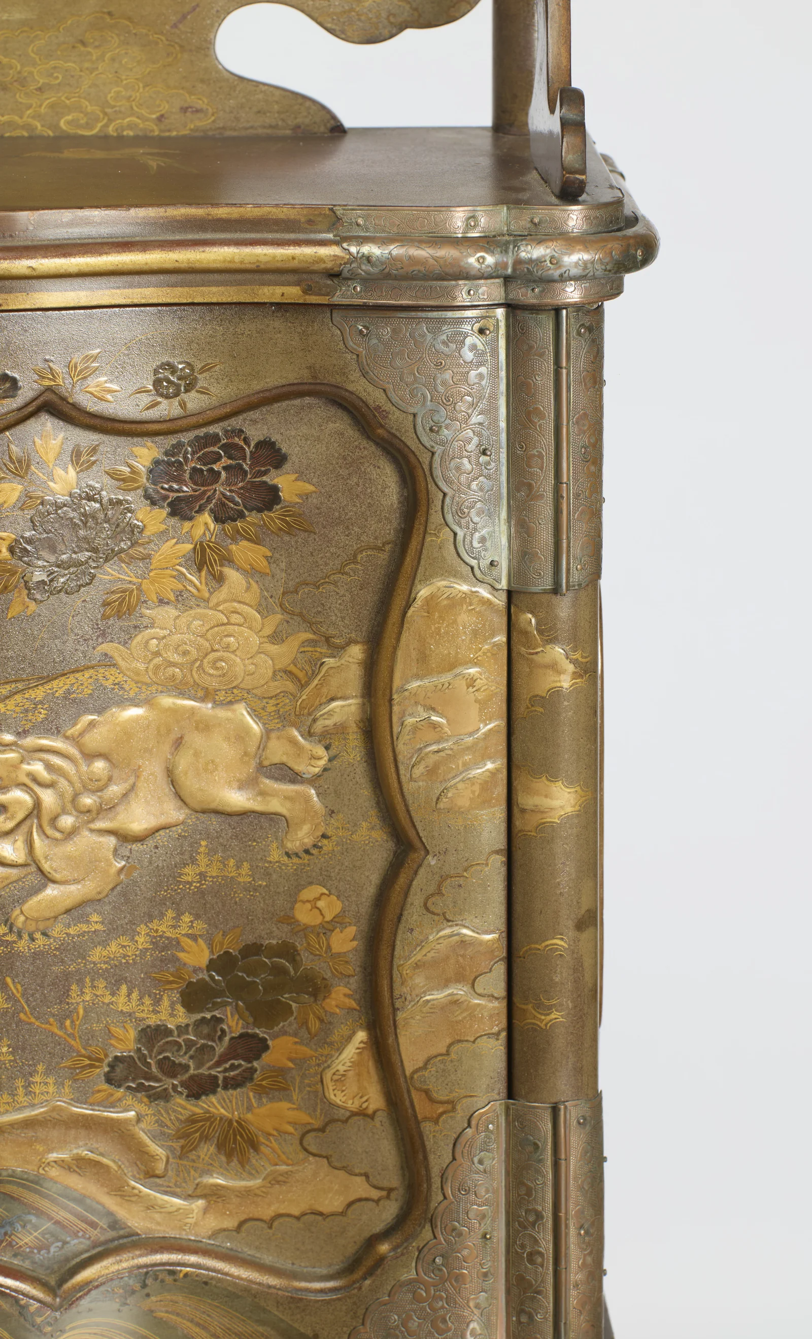 Engraved metal corner plates and hinges framing a maned lion bounding past peonies worked in gold and silver relief.