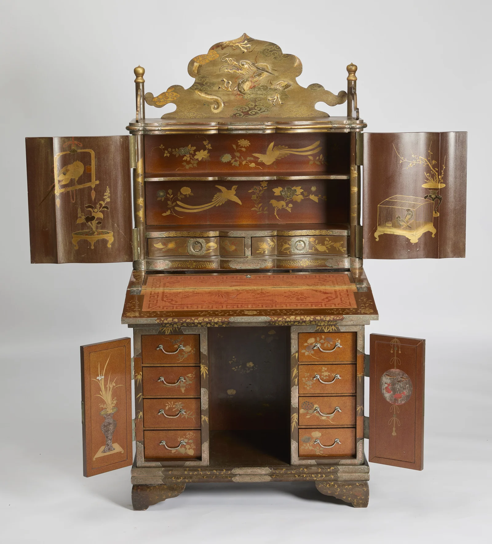 Upper doors, fall-front and lower doors all open, revealing the red-lacquered interior, the fabric-lined writing surface and twin banks of four drawers.