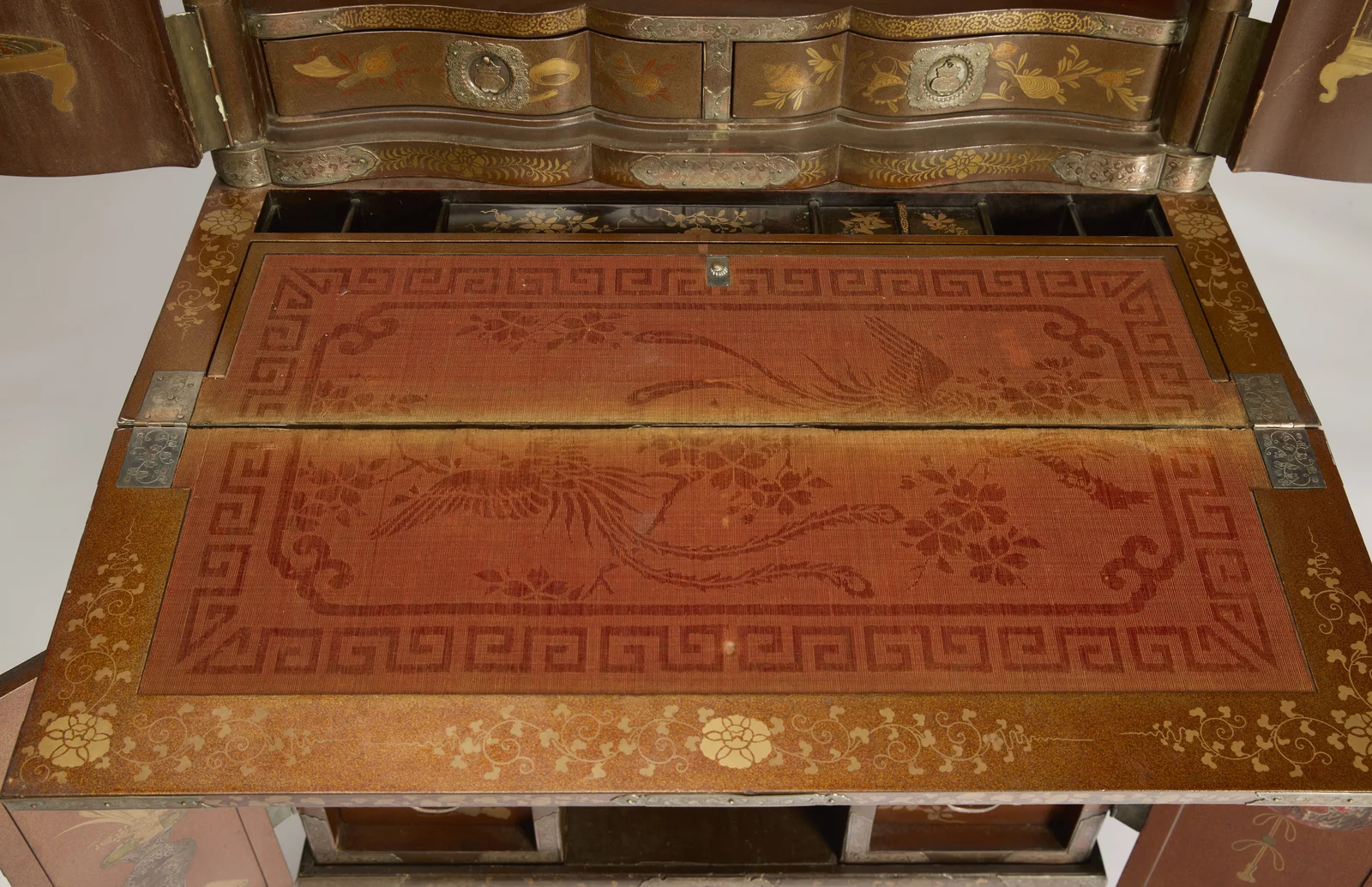 Two serpentine drawers with engraved mounts above the writing surface, the fabric woven with long-tailed birds inside a key-fret border.