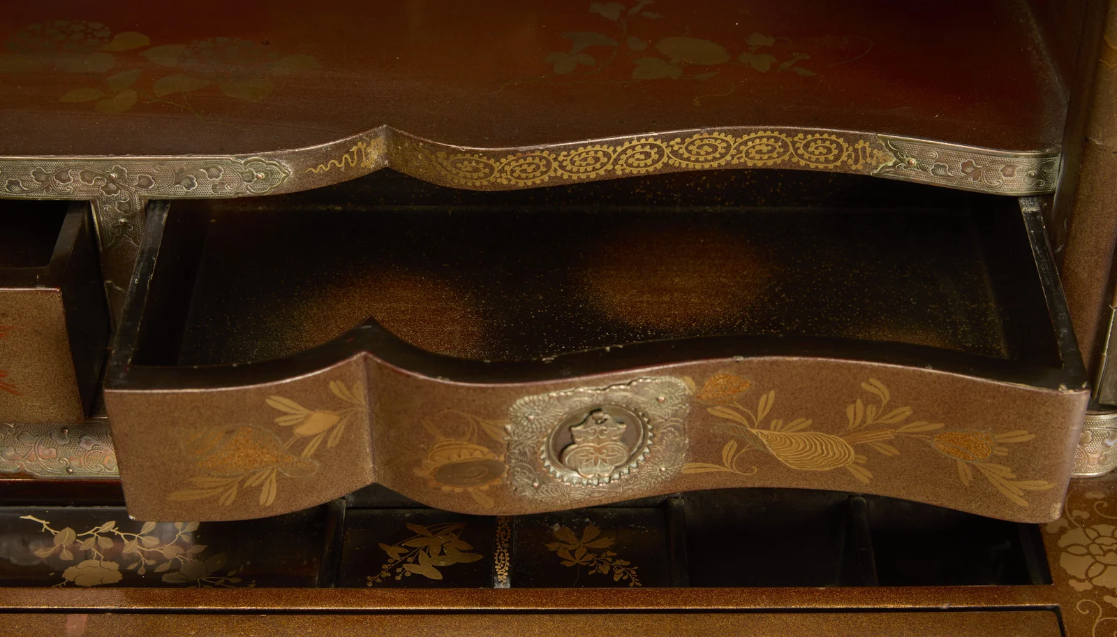 The serpentine drawer pulled open, its interior finished in black with gold speckling, open compartments visible beneath.