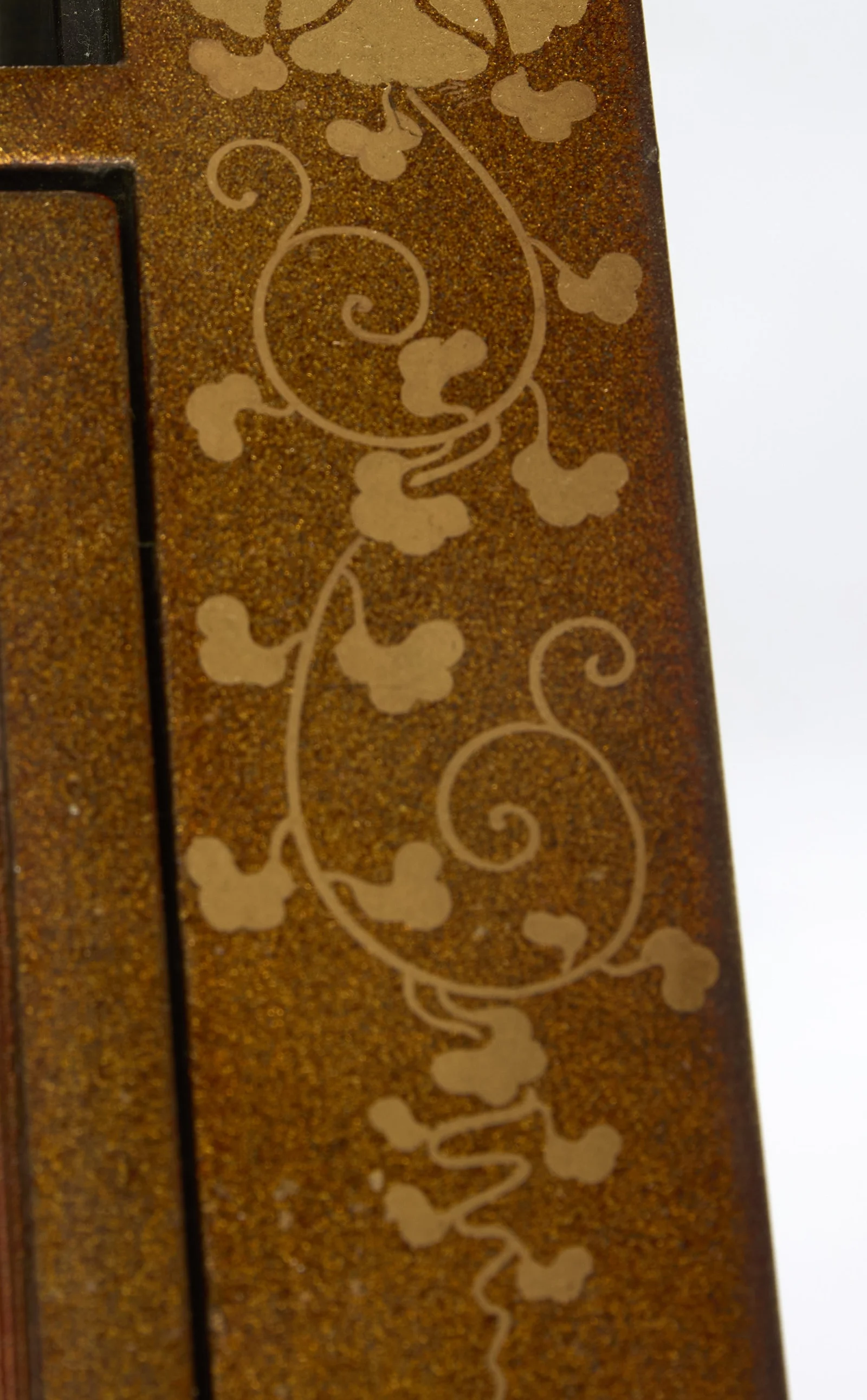 The key-fret border of the fabric meeting gilt peony scrolls on the surround, open wells behind, with wear visible along the door edge above.