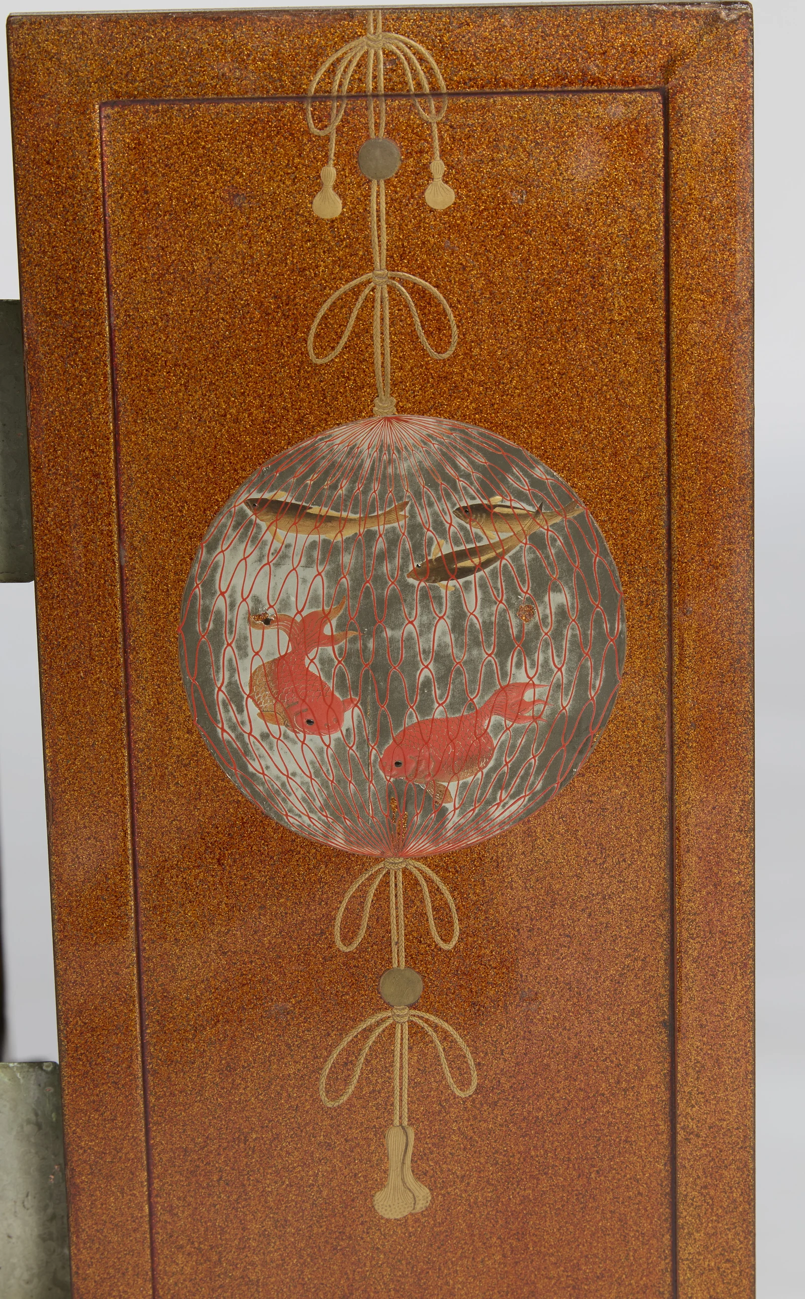 A globe of red netting holding goldfish and small fish, hung from looped and tasselled cords on the sparkled ground.