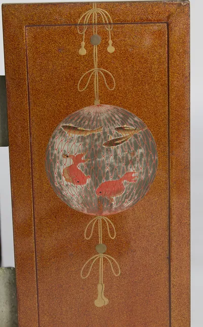 A globe of red netting holding goldfish and small fish, hung from looped and tasselled cords on the sparkled ground.