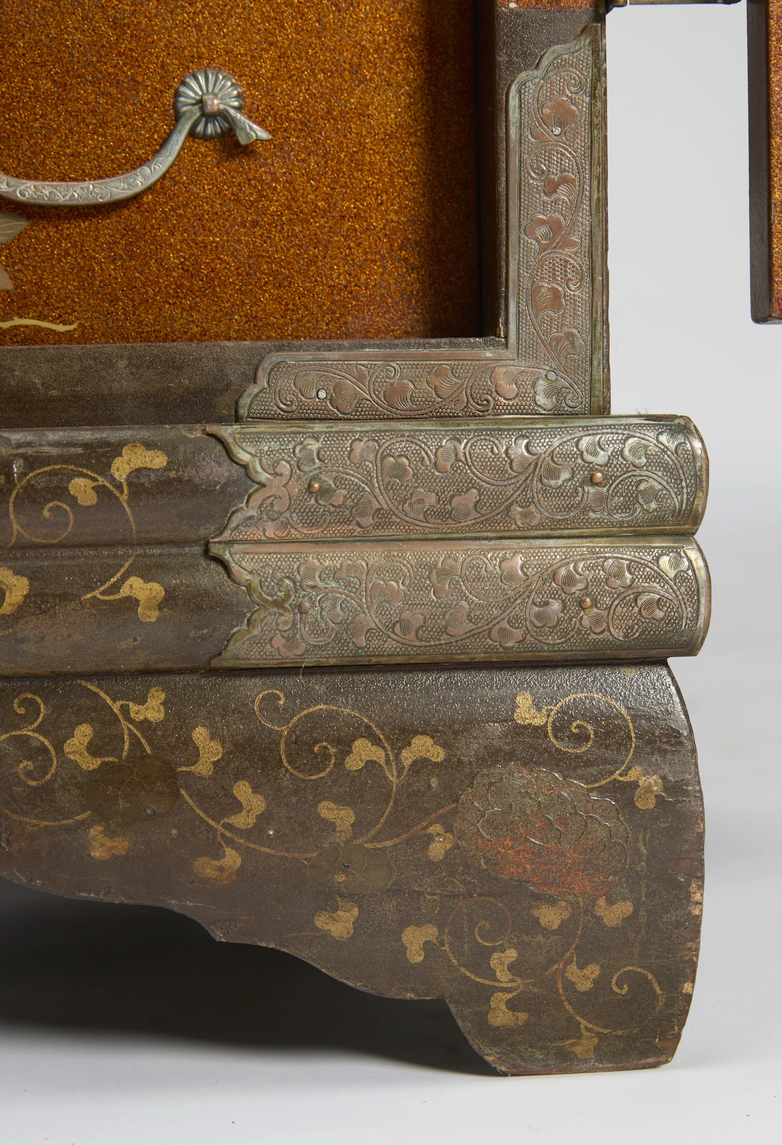 Engraved corner plates meeting at the plinth below a drawer with silvered handle, the shaped foot showing wear at its edge.