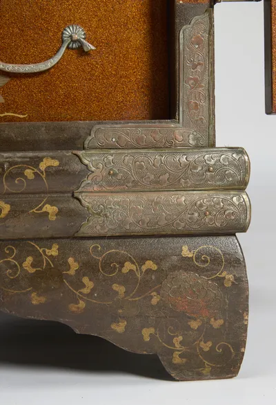 Engraved corner plates meeting at the plinth below a drawer with silvered handle, the shaped foot showing wear at its edge.