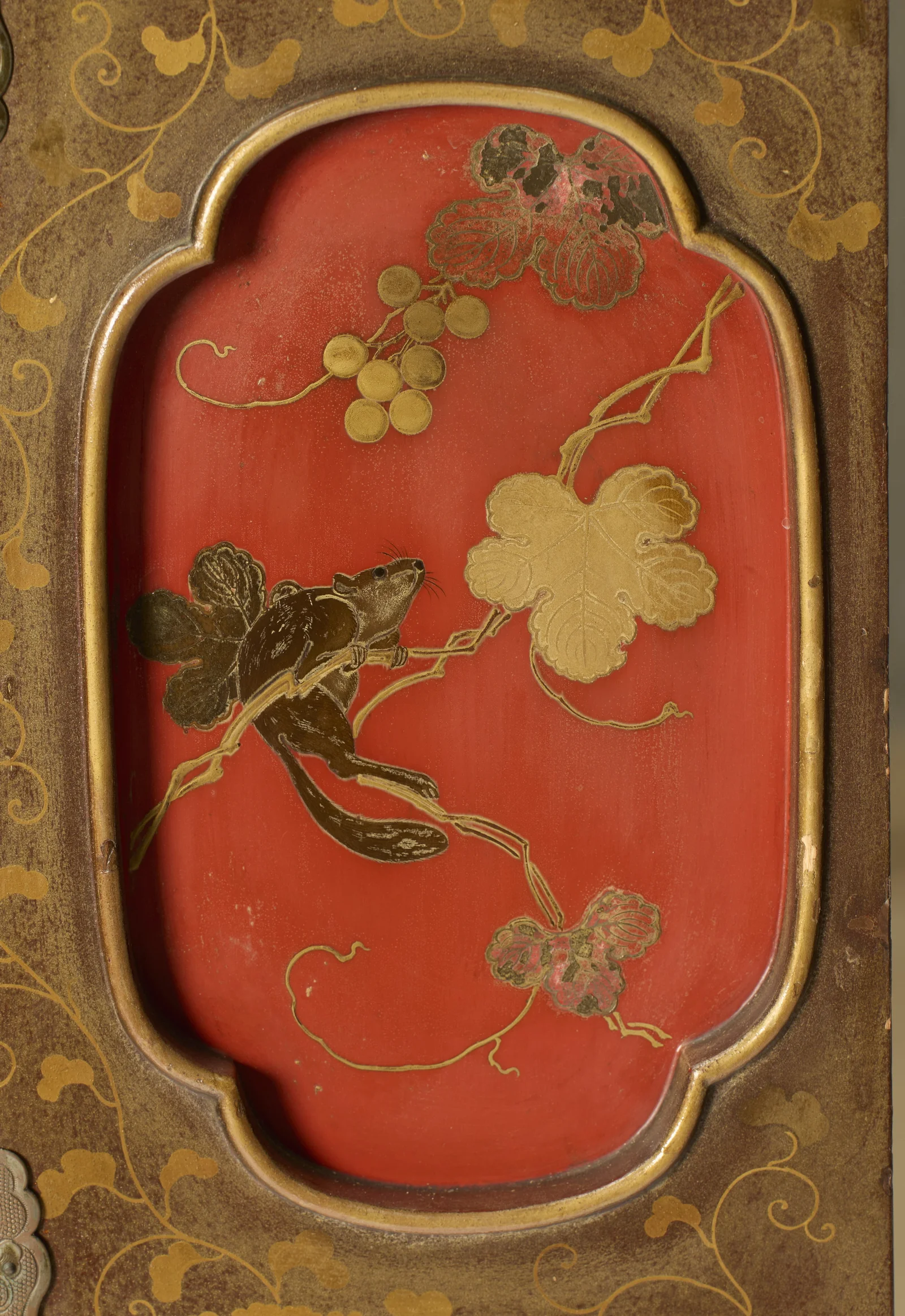 A squirrel climbing a fruiting vine with berries and broad leaves, set in a gilt-edged red reserve amid scrolling vines.