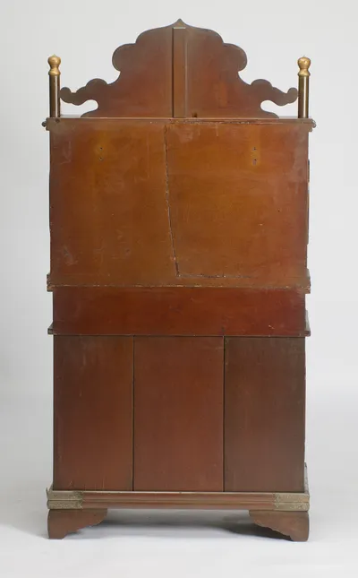 The back finished in plain russet-brown lacquer, showing the crest silhouette, turned finials and metal-bound plinth, with scattered scuffs and scratches.