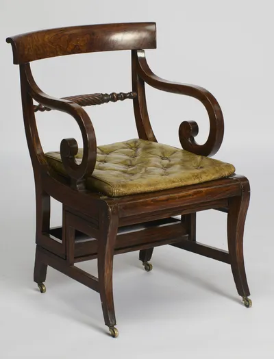 Deep scrolled arms and a buttoned leather squab beneath the broad figured crest rail, with the spiral-turned cross rail behind and brass castors at each foot.