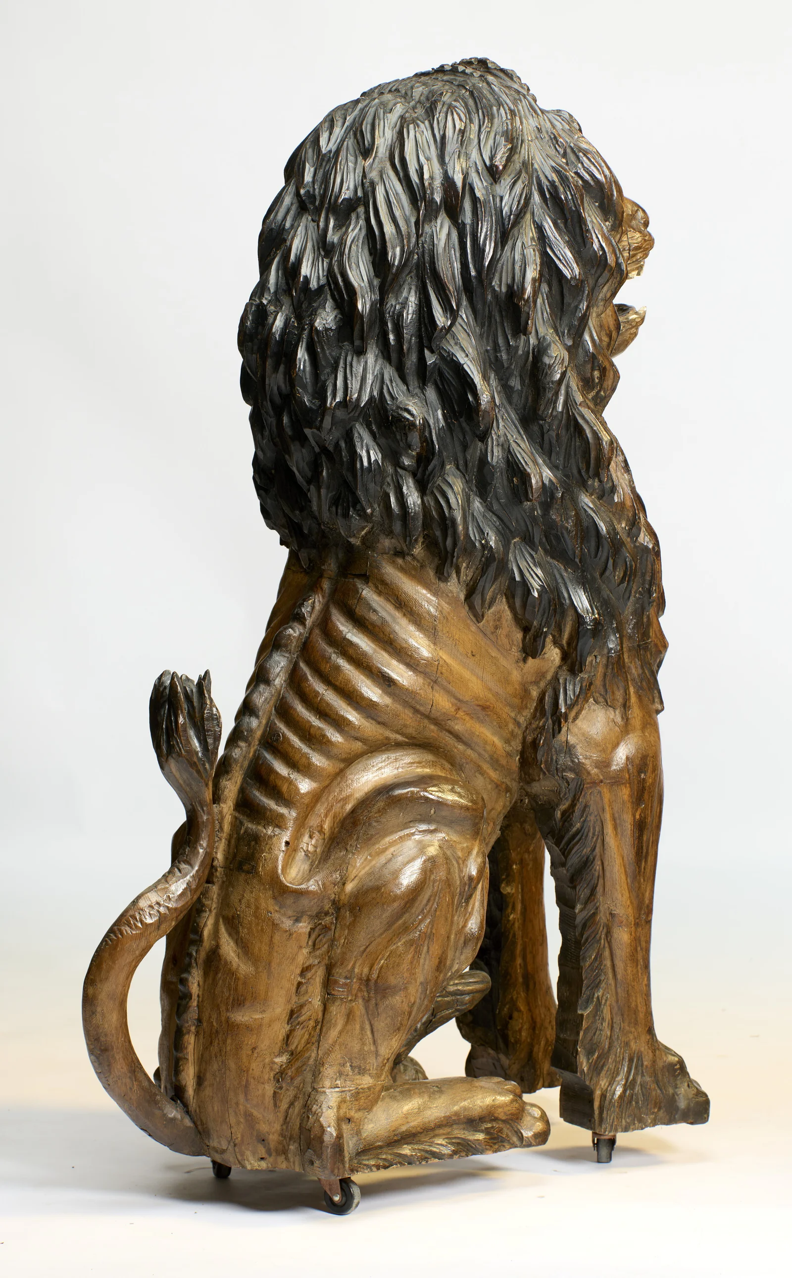 Ribbed carving sweeps around the flank, and the tail curls up to a leaf-shaped tuft against the hindquarters.
