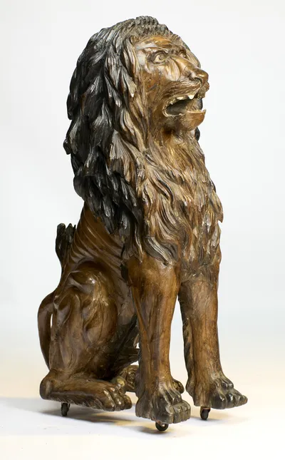 The whole lion seated with head raised and jaws open, the mane cut in deep locks that spill over the chest and shoulders.
