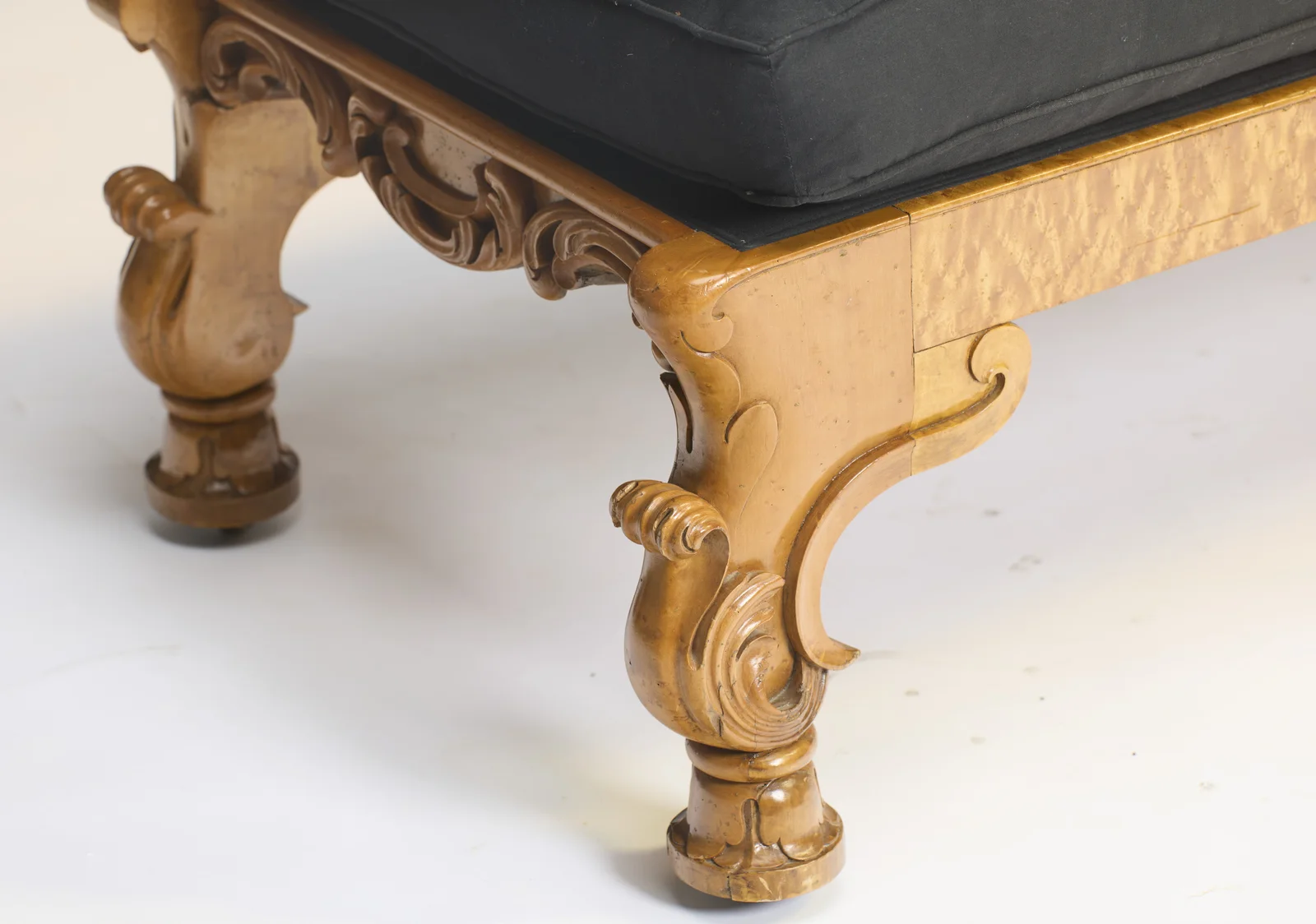 Two scroll-carved bracket legs with leafy flourishes meet a rail veneered in tight speckled figure, each foot turned and set on a castor.
