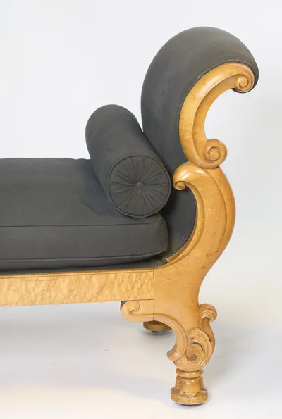 The deep volute of the crest curls over the bolster's pleated rosette end, with sprays of carved leafwork on the support below.