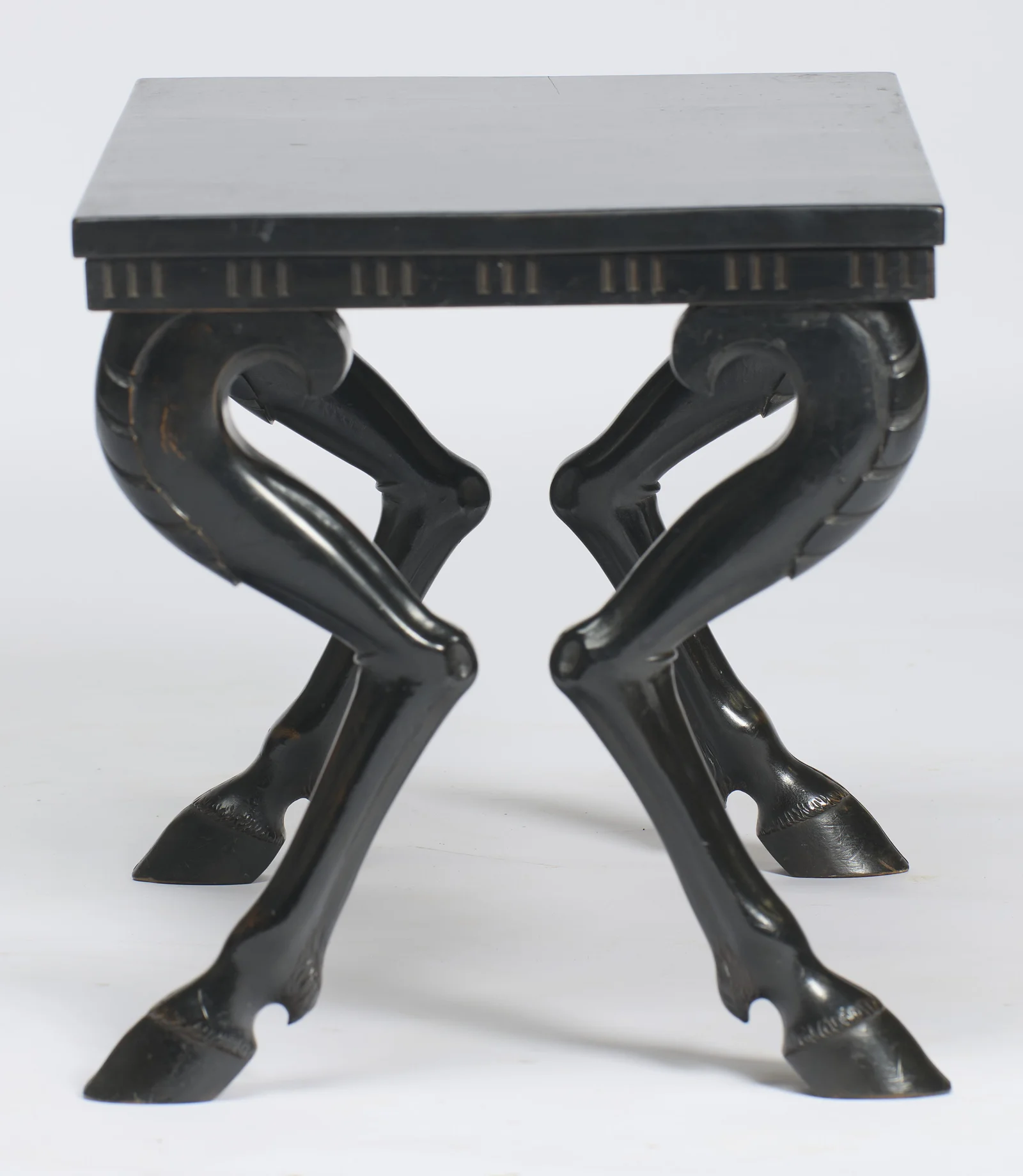 From the short side the legs cross in matched pairs, each shank tapering through a carved hock to a cloven hoof.