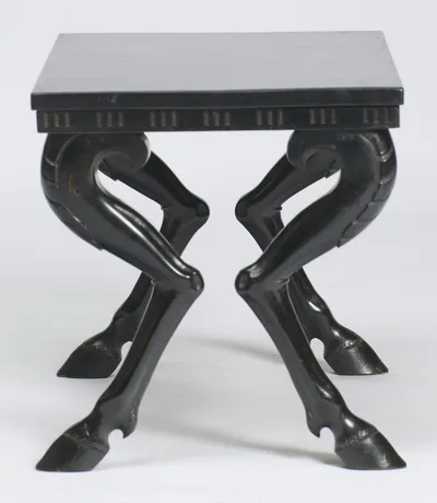 From the short side the legs cross in matched pairs, each shank tapering through a carved hock to a cloven hoof.