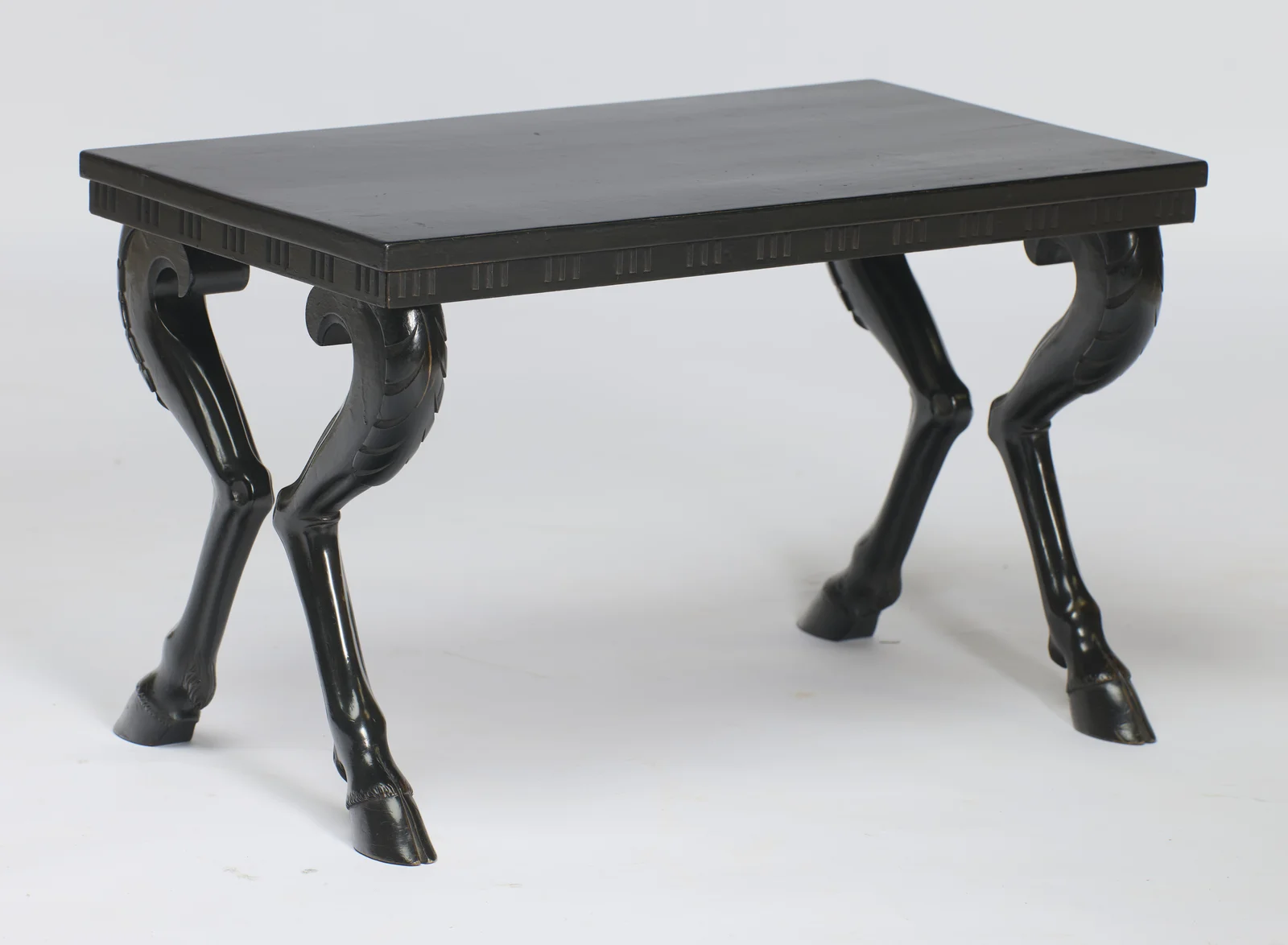 The rectangular black top overhangs a flute-carved frieze and is carried on four splayed animal legs ending in cloven hooves.