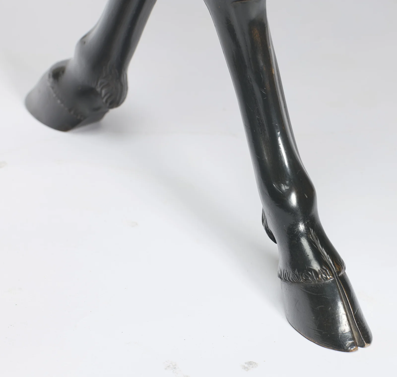 The foot is carved as a cloven hoof beneath a tuft of hair, with wear to the finish along the toe.