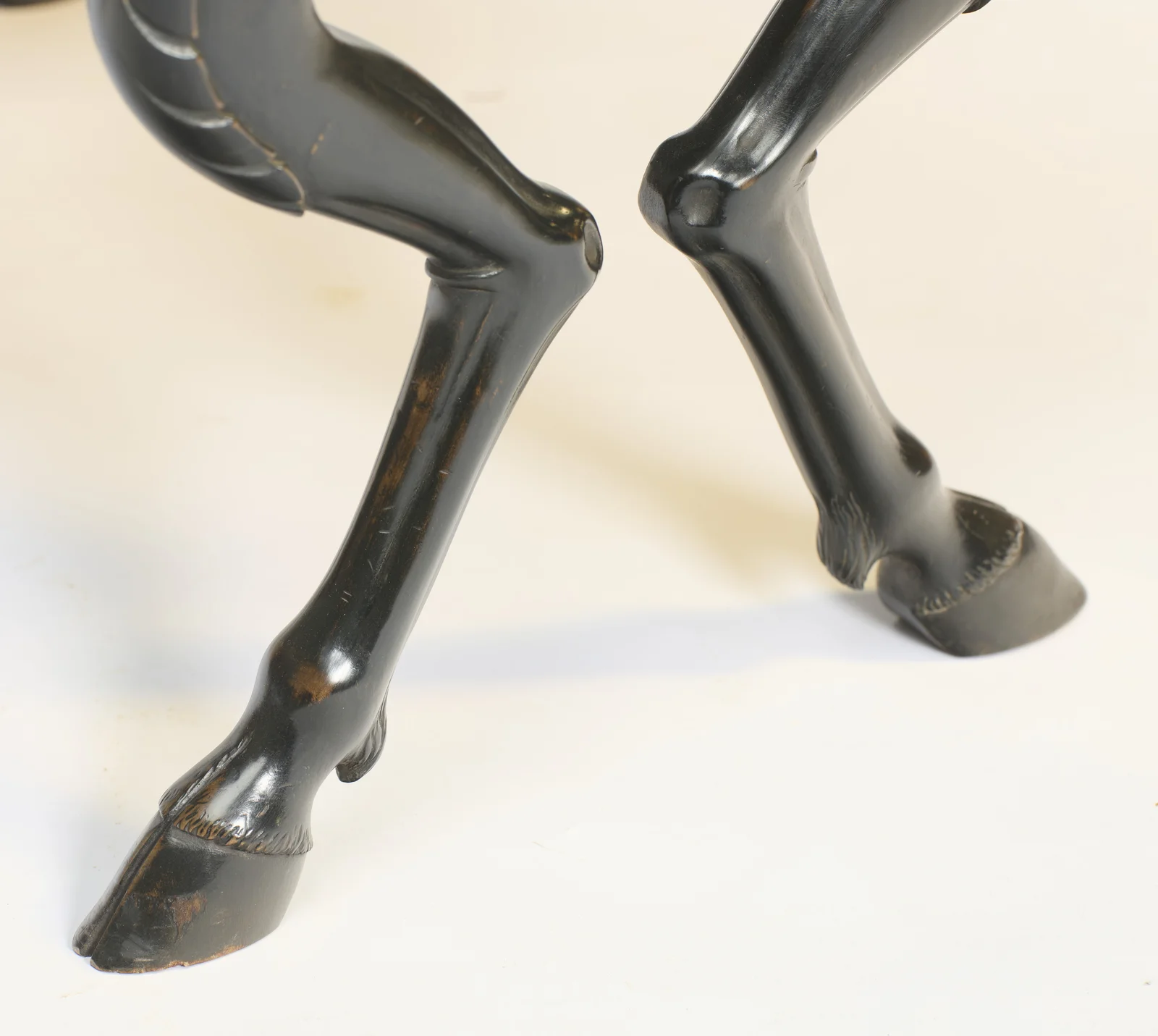 Each leg angles back at the hock and tapers to a split hoof with a fringe of carved hair at the pastern.