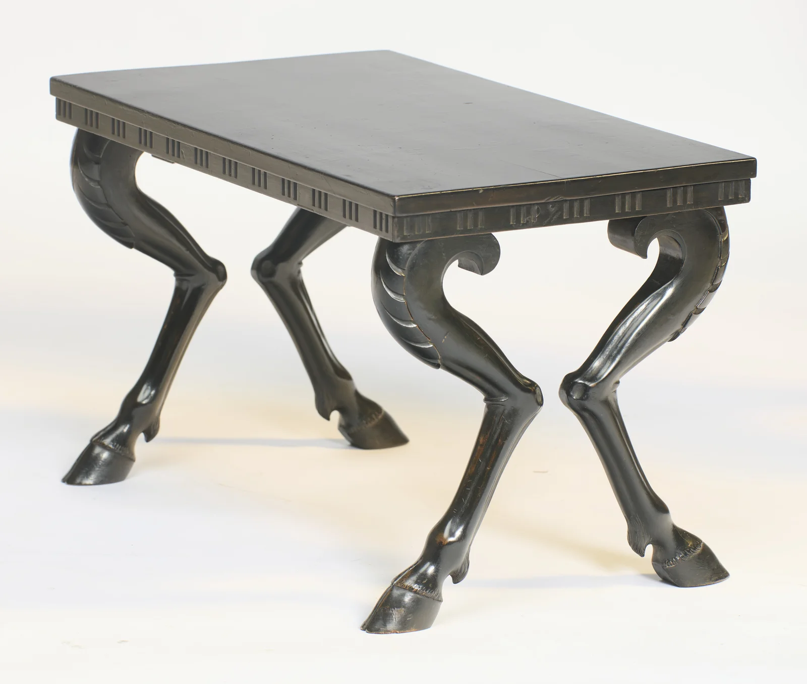 The top recedes to show the legs kicking outward in pairs, each haunch curling into a scroll beneath the frieze edge.