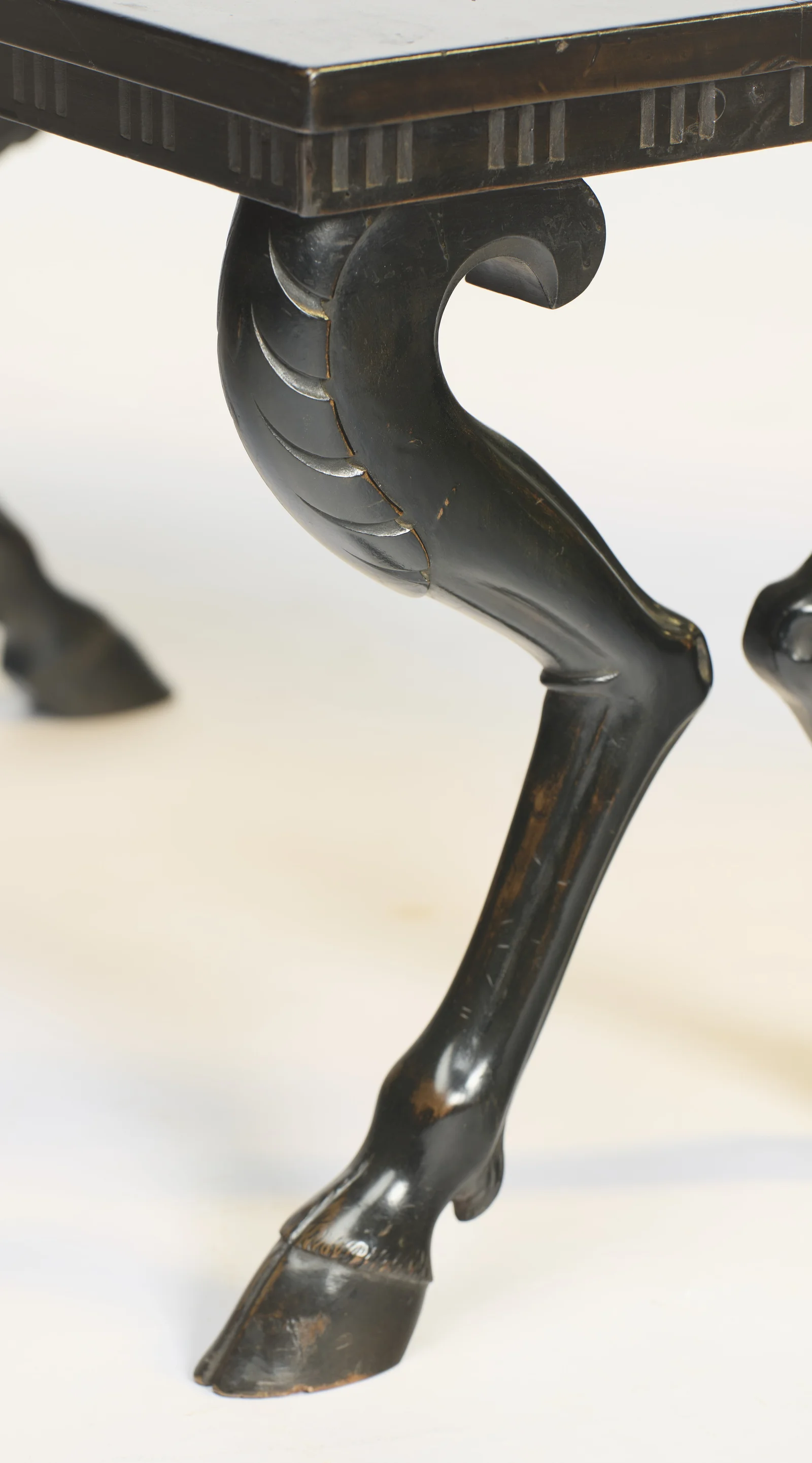 The haunch is carved with overlapping feather-like lappets rising to a tight scroll, the black finish lightly rubbed through on the high edges.