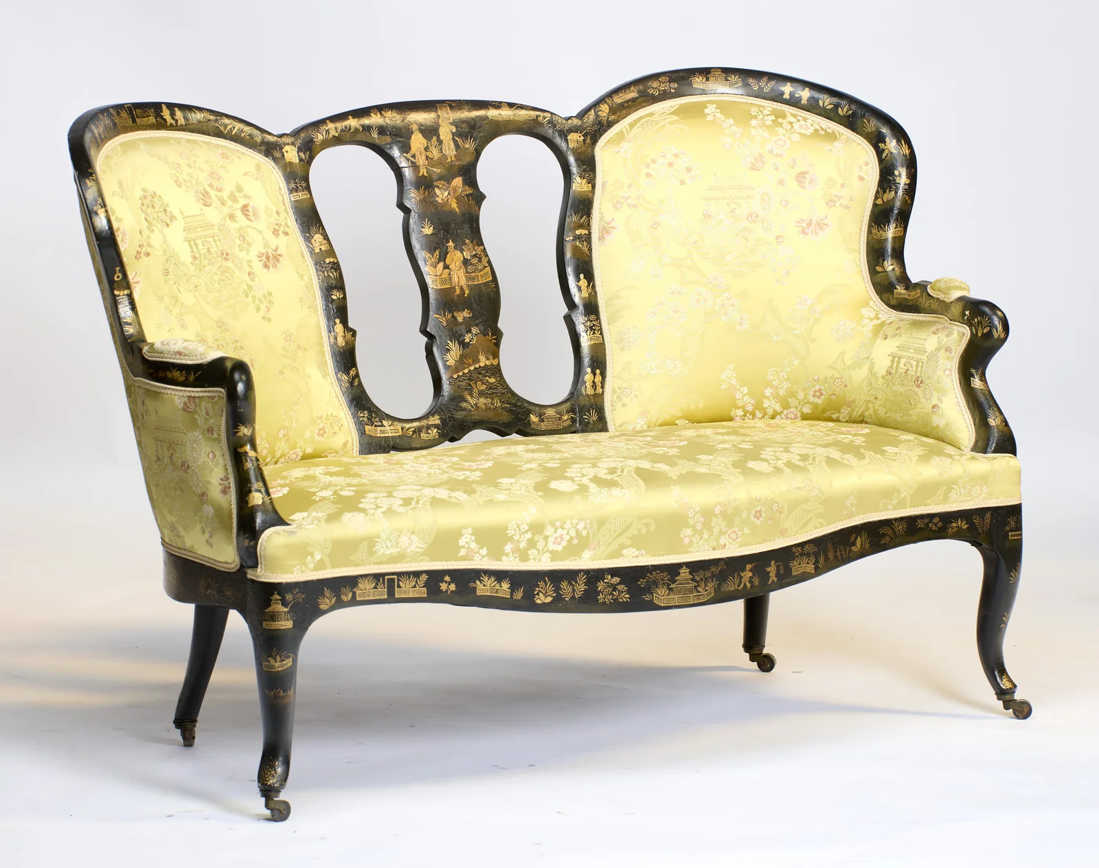 The scrolled arm and shorter back stand nearest, with the taller winged back rising beyond the pierced splat.