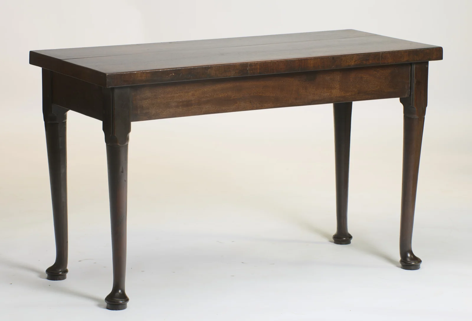 The table at an angle, showing the overhanging two-board top, the deep plain frieze and all four turned legs with their pad feet.