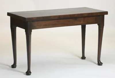 The table at an angle, showing the overhanging two-board top, the deep plain frieze and all four turned legs with their pad feet.