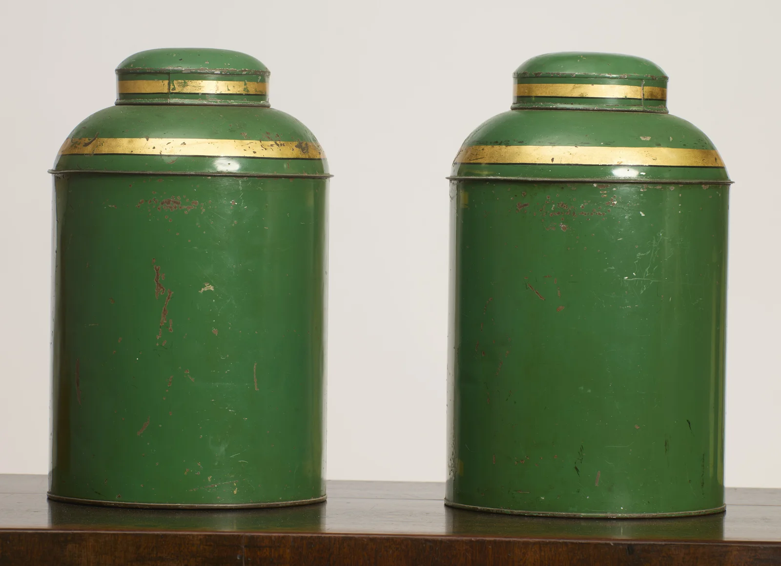 The backs are plain green below the gilt shoulder and cover bands, with scattered chips, scratches and rubbing through the paint to a reddish ground.