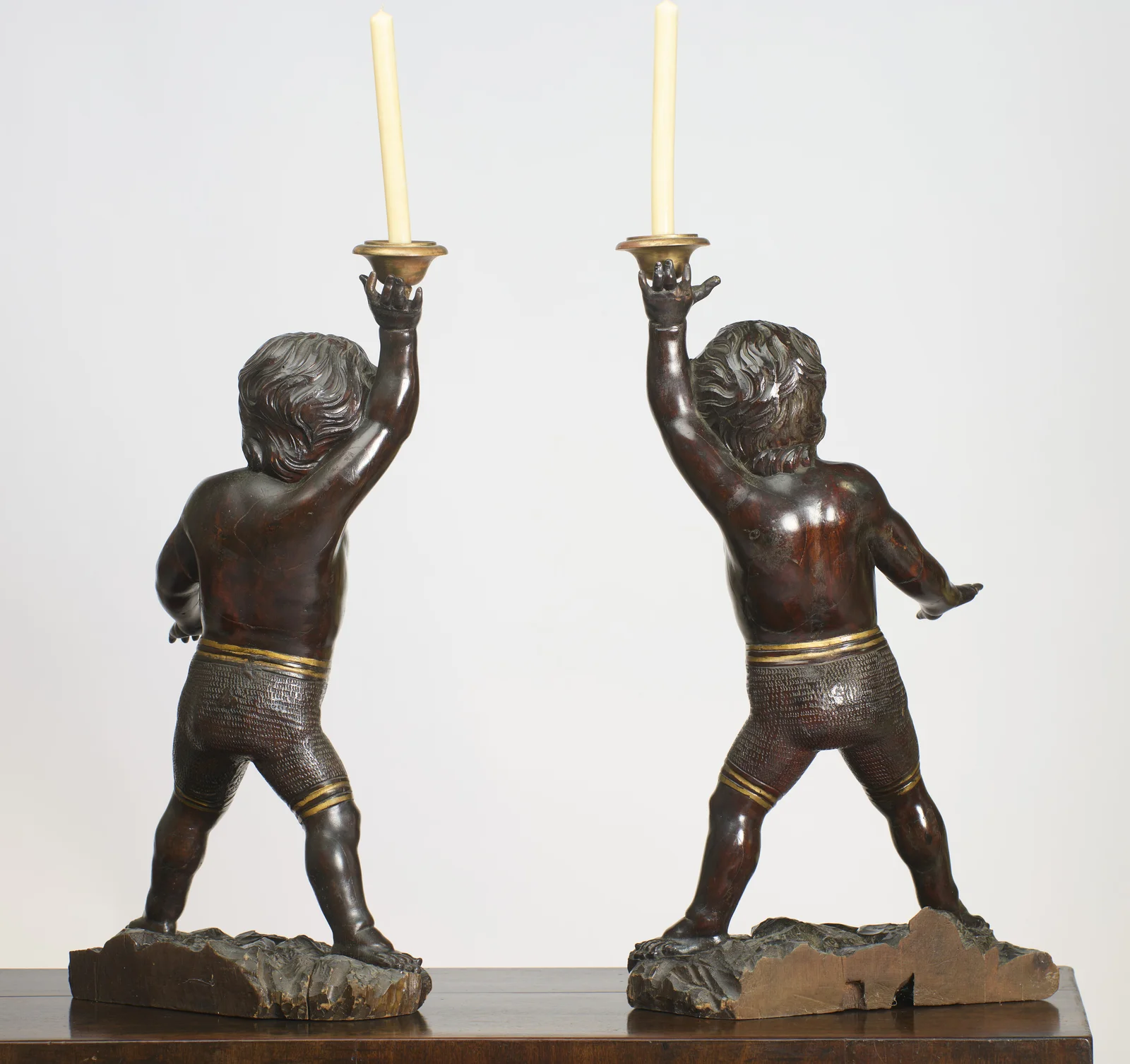 The backs of both figures with the gilt waistbands carried round; bare timber and an open split show at the rear of the rockwork bases.