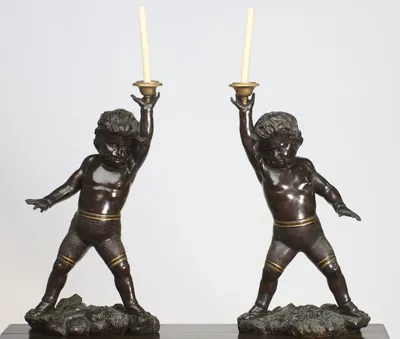 Both figures stride across carved rockwork bases in mirrored poses, each raising a gilt-metal drip-pan and nozzle overhead on an open palm.
