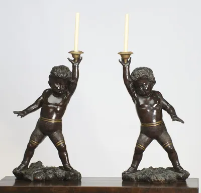 Both candlesticks complete from candle tip to carved base, standing on a polished tabletop and closely matched in height and stance.