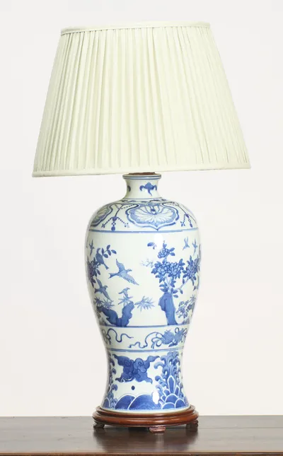 The whole lamp seen straight on, birds in flight among flowering branches across the body, raised on a turned wood base beneath a pleated cream shade.