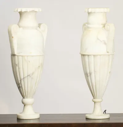 Both urns stand full height on a dark wooden surface, the crimped and fluted rims above the scroll handles, with a braided flex just visible at the right-hand foot.
