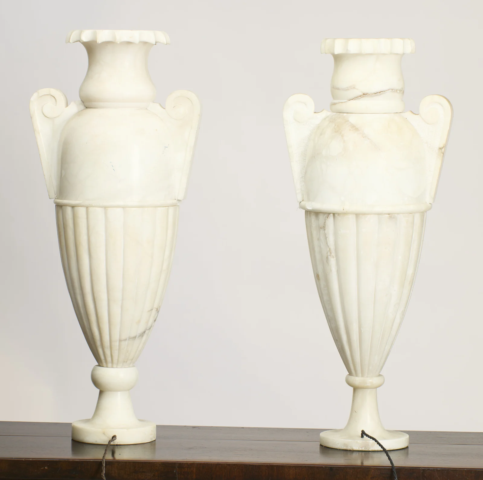 Pronounced grey veining crosses the neck and shoulder of the right-hand urn, whose panels between the handles show a stippled texture against the smooth left-hand urn.