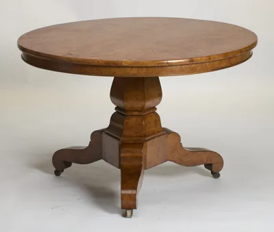 Circular top with dense burr figuring, raised on a faceted baluster pedestal with three scroll legs ending in castors.