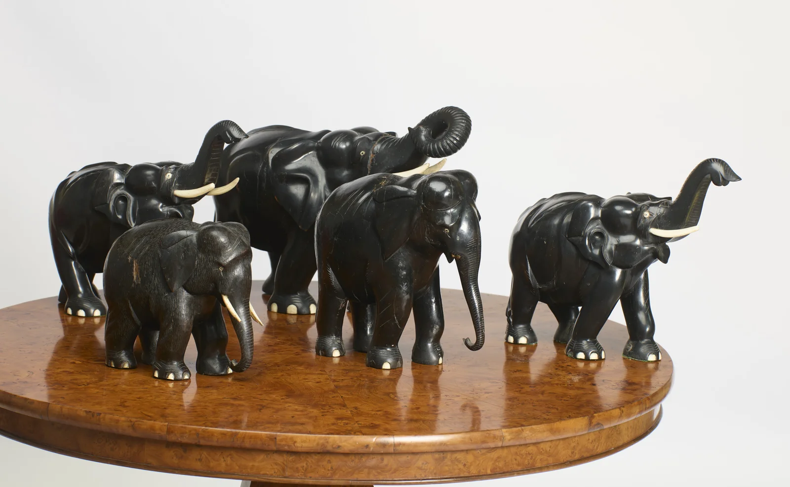 A graduated set of five carved black elephants with inset pale tusks and toenails, grouped on the table top.