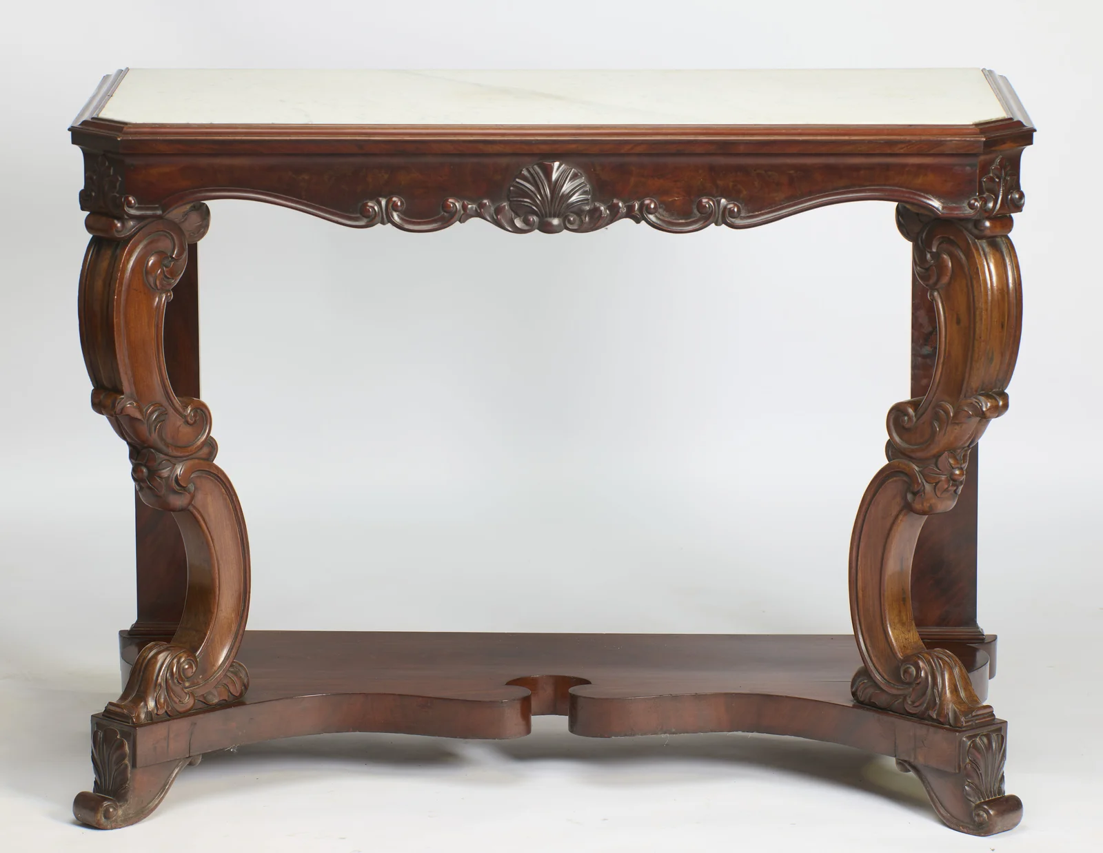 The white marble top with canted front corners sits above a serpentine apron centred by a carved shell, raised on scrolled supports over a shaped platform base.
