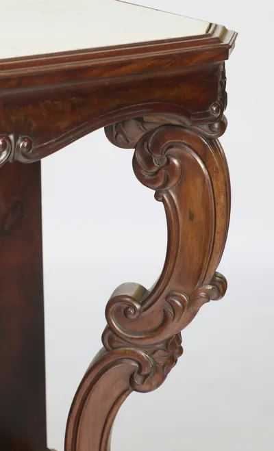 The moulded C-scroll of the support carries carved leafage where it meets the canted corner of the apron beneath the marble.
