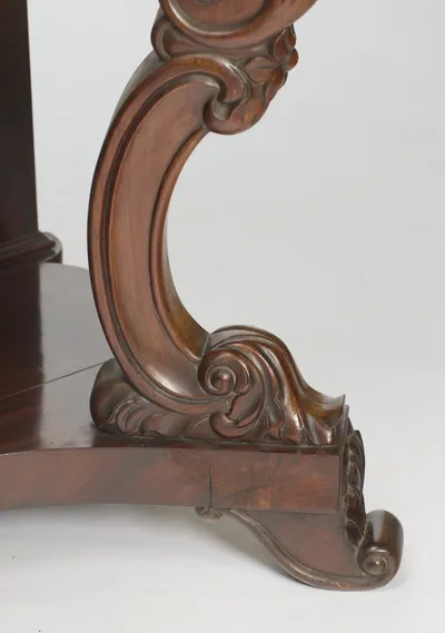 The scroll of the support ends in an acanthus-wrapped foot beside a scrolled toe on the platform base, with old cracks visible on the plinth face below.