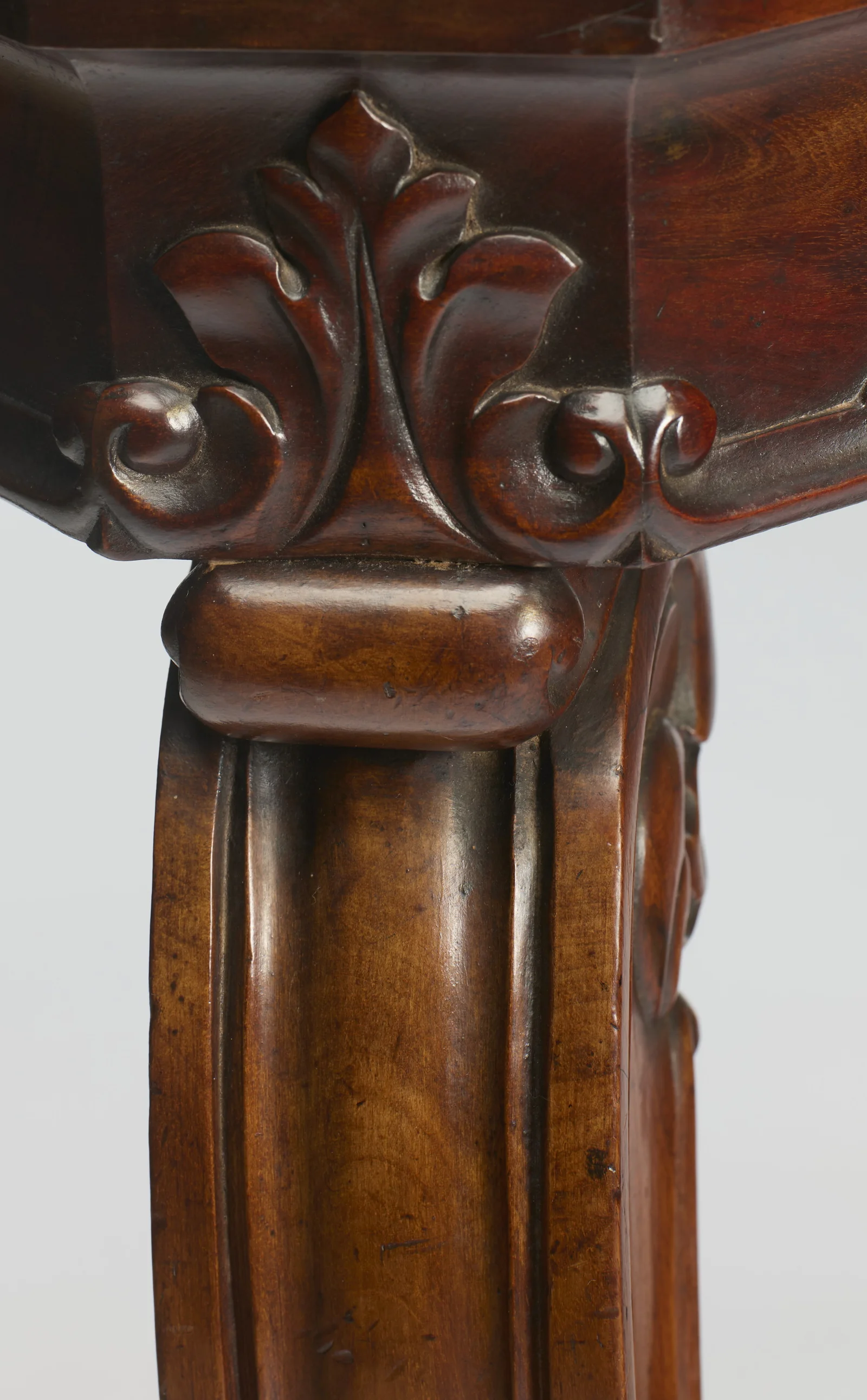The canted corner of the marble sits within a moulded wood edge above a crisply carved leaf ornament at the head of the leg.