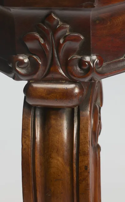 The canted corner of the marble sits within a moulded wood edge above a crisply carved leaf ornament at the head of the leg.